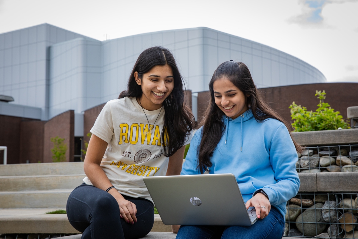Two students smile while looking at a laptop t