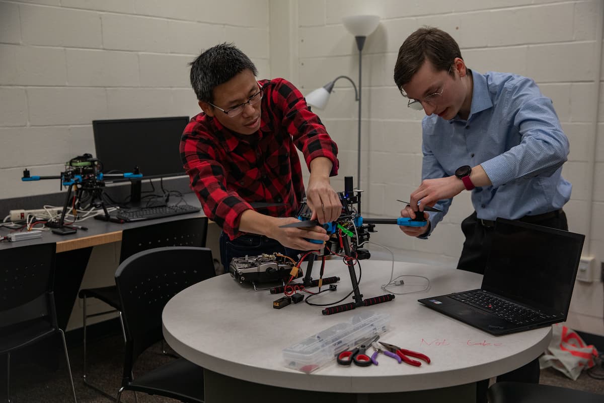 two individuals working on a drone at a table in a lab