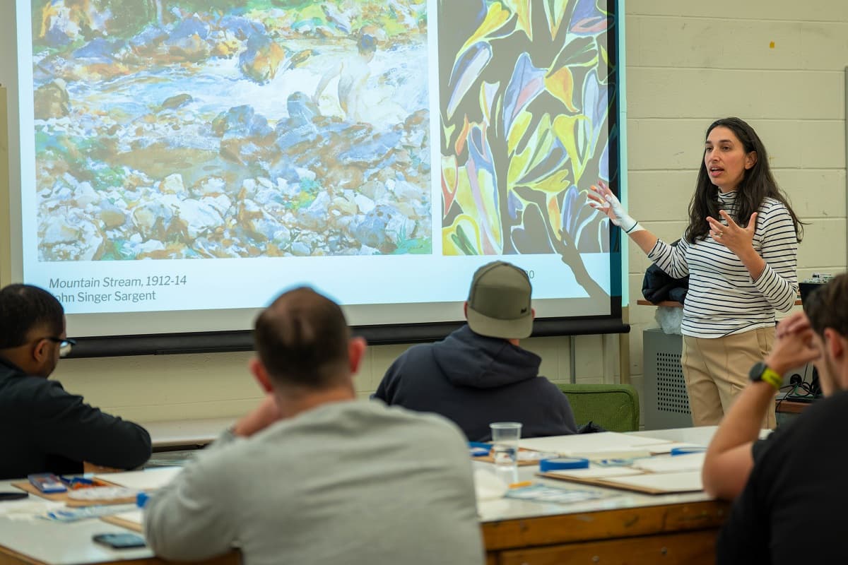 an art history teachers next to a projector screen lectures students