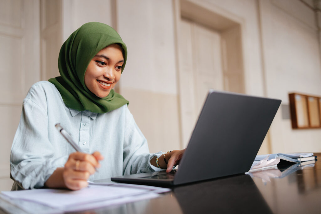 A student smiles while looking at their laptop.
