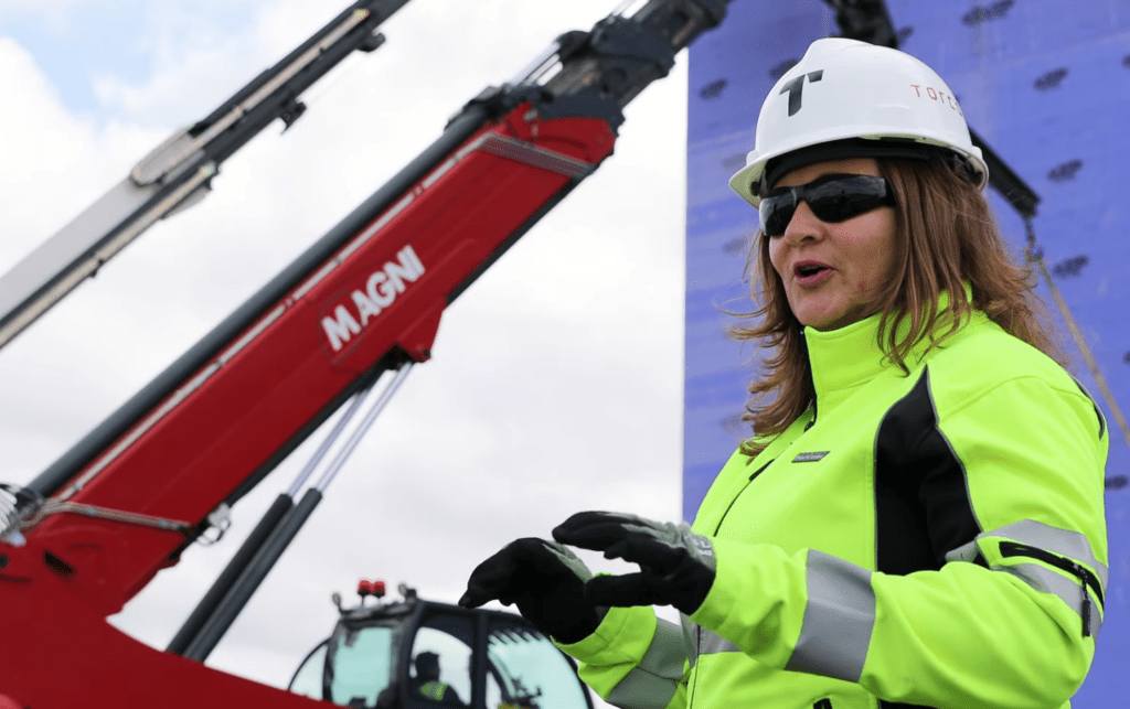 A construction worker is speaking while near construction equipment.