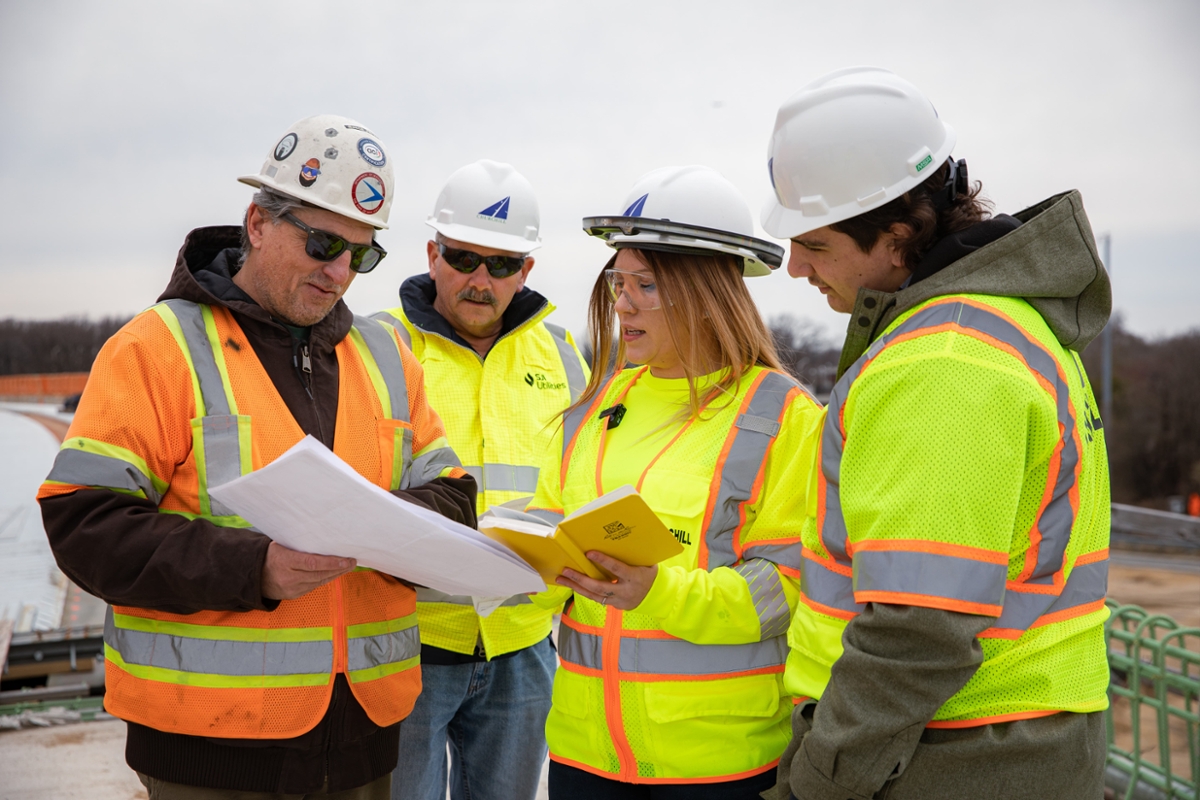 A group of construction workers chatting while looking at a plan out at a construction site.