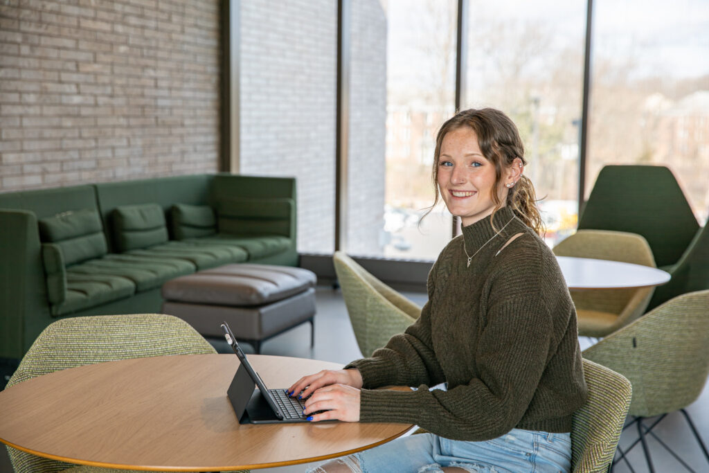A student smiles while on their tablet at a table.
