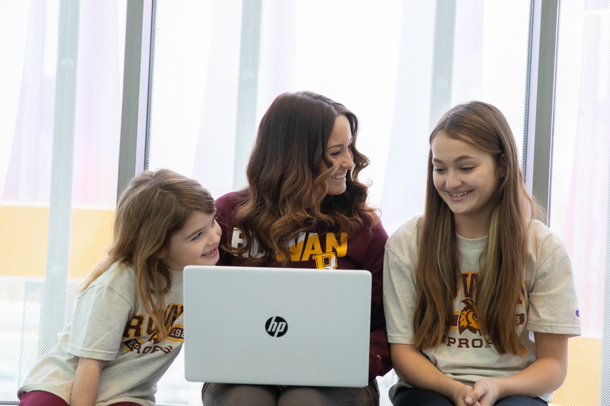 An adult student sits at a laptop next to her two children.
