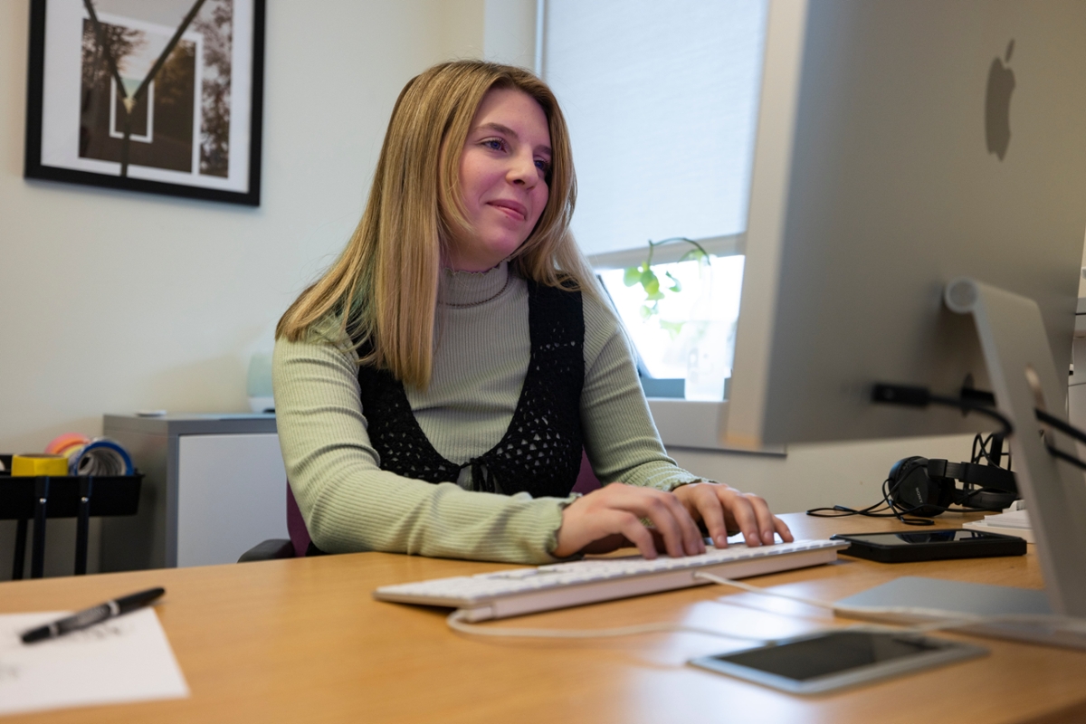 A student smiles while looking at a desktop computer.