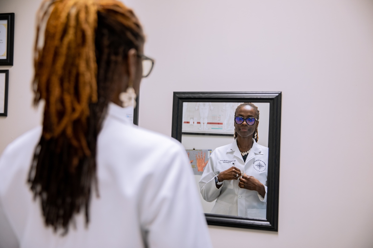 A student looks into a mirror while adjusting their white coat.