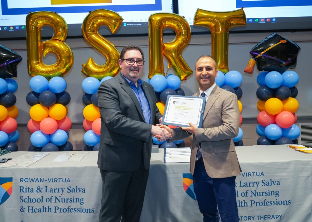A student receives an award in front of a balloon banner that spells BSRT,