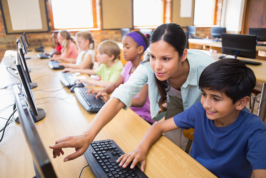 A teacher helps a student on the computer in a classroom.