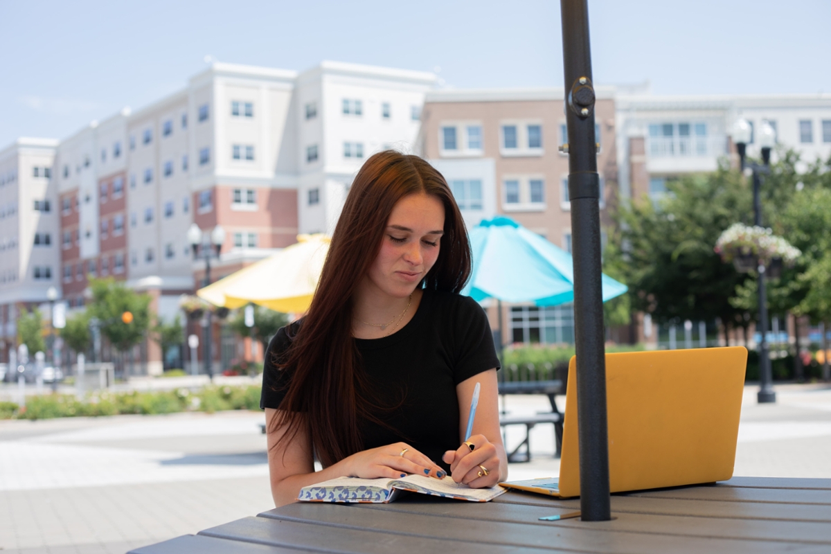 A Rowan student writes something down in a notebook at a picnic table on Rowan's main campus in Glassboro, NJ.