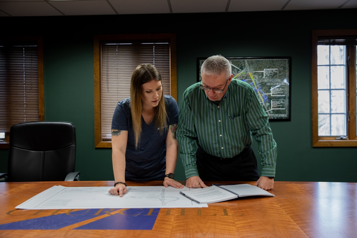 Two individuals stand in an office looking at construction plans in an office.