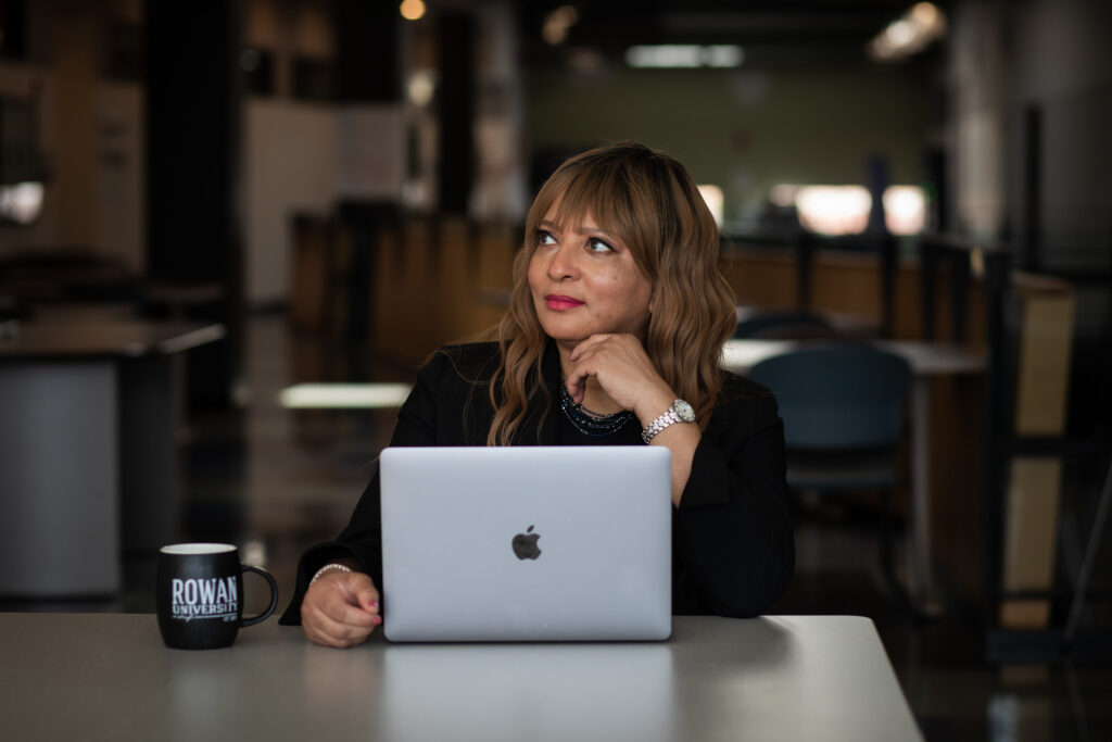 A Rowan student sits at a table with their laptop and a Rowan mug.