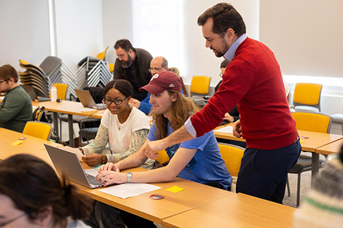 professor in classroom helping students on laptop